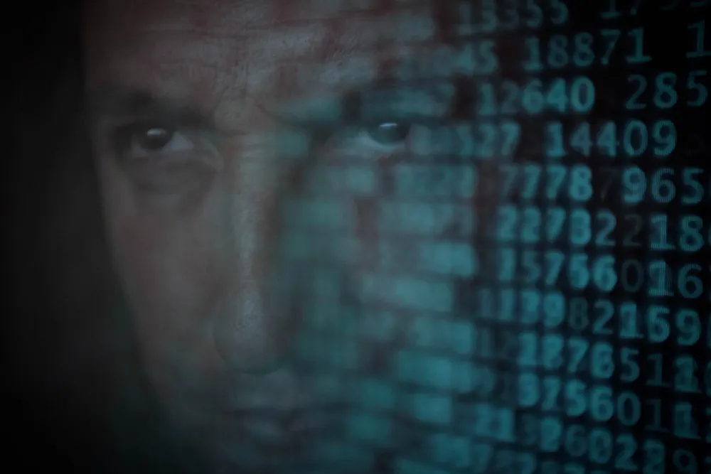 Data Breach: The Aftermath - Image shows a close up portrait of an adult male against a black background with binary code in front of him