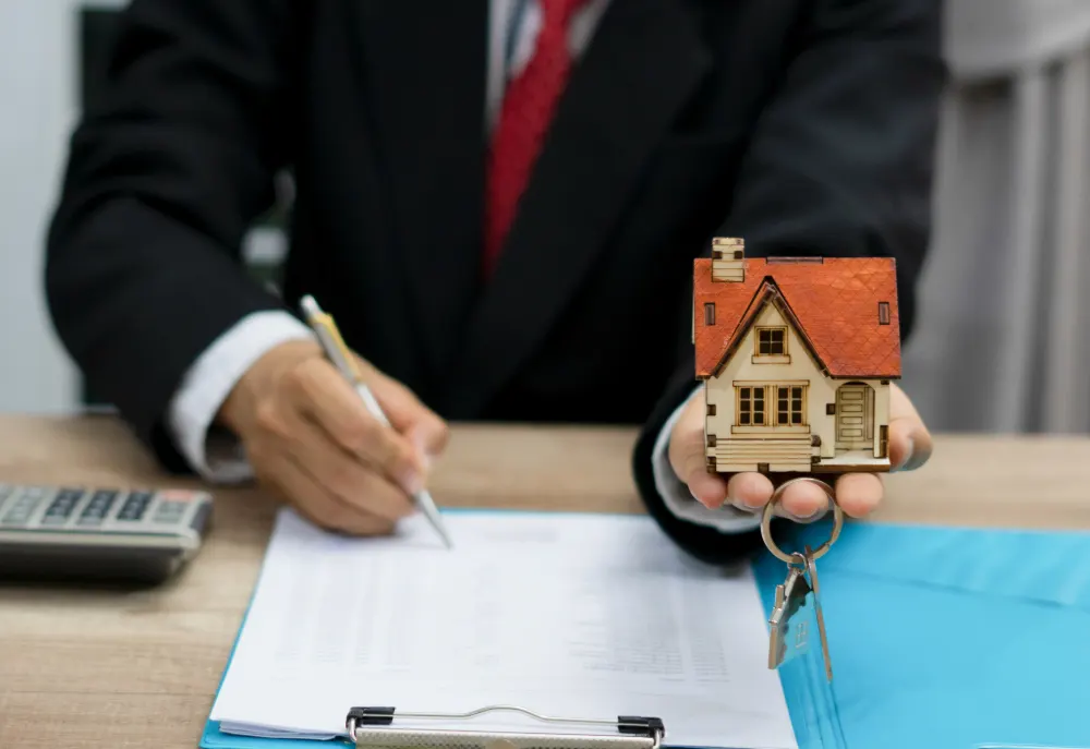 Mortgage Prisoners featured image. Salesman holding a house in his hands with a set of keys filling out a form